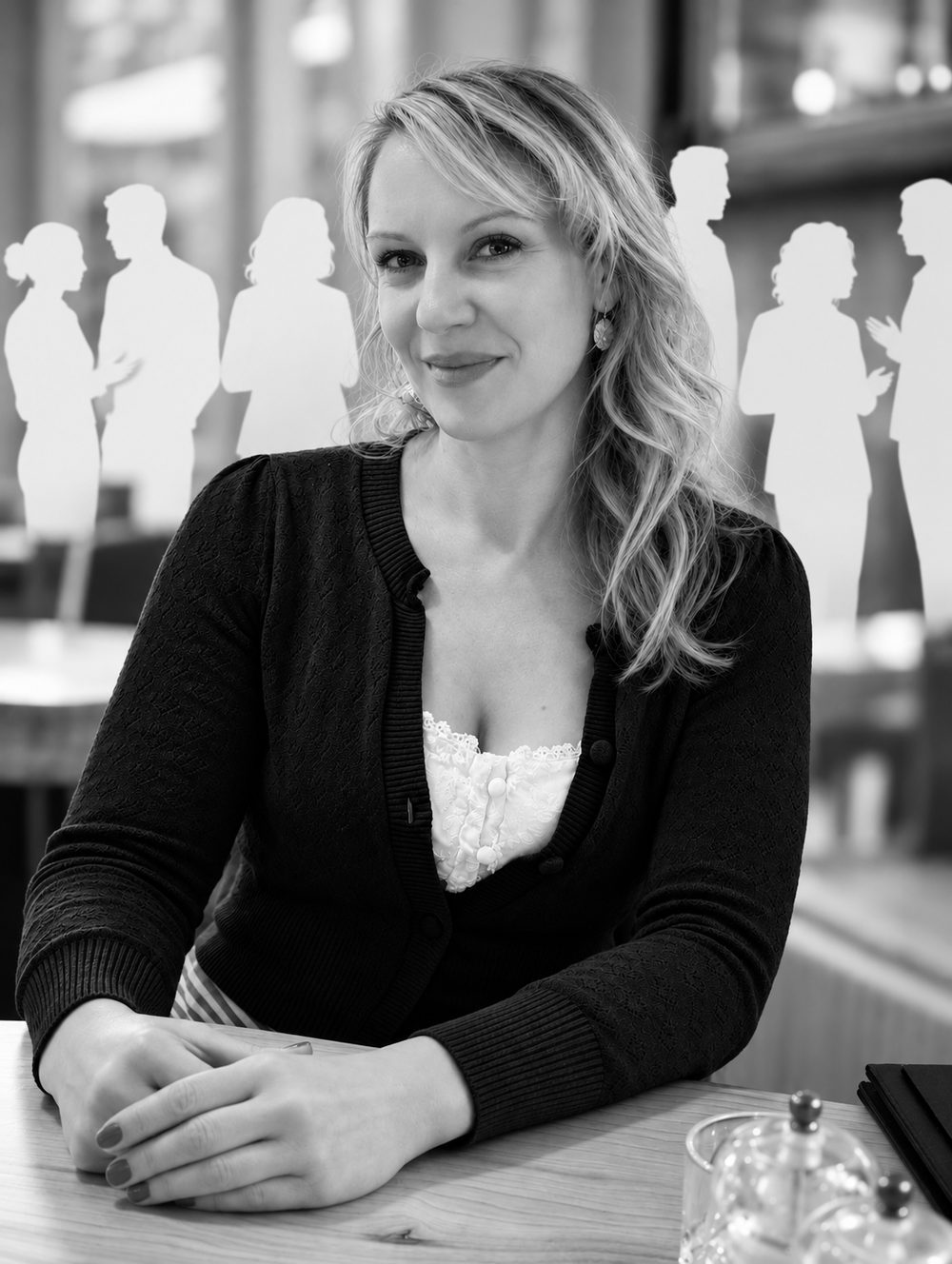 Bettina Kochheim sitzt an einem Tisch. Hinter ihr stehen weiße Silhouetten von Menschen im Gespräch, ein Sinnbild für ihr Netzwerk.
